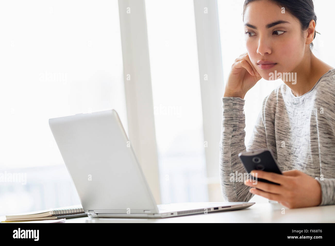 Hispanic woman using cell phone and laptop Stock Photo
