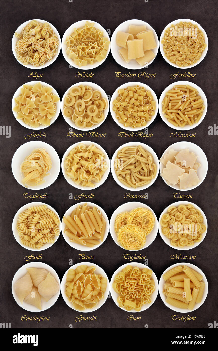 Large pasta dried food selection in round bowls over brown lokta paper background with titles. Stock Photo