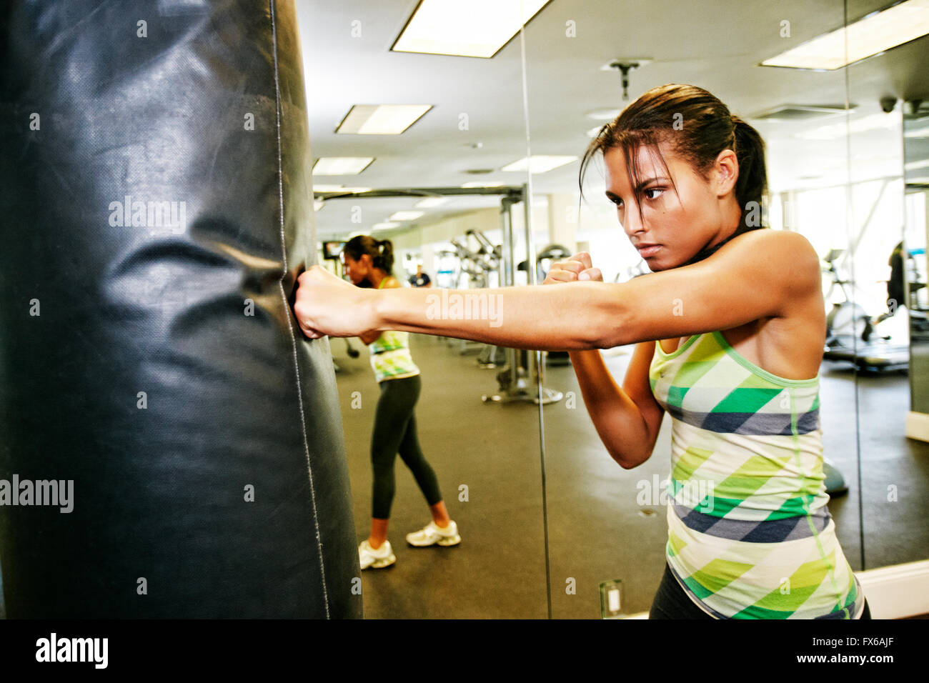Mixed race woman hitting punching bag in gymnasium Stock Photo