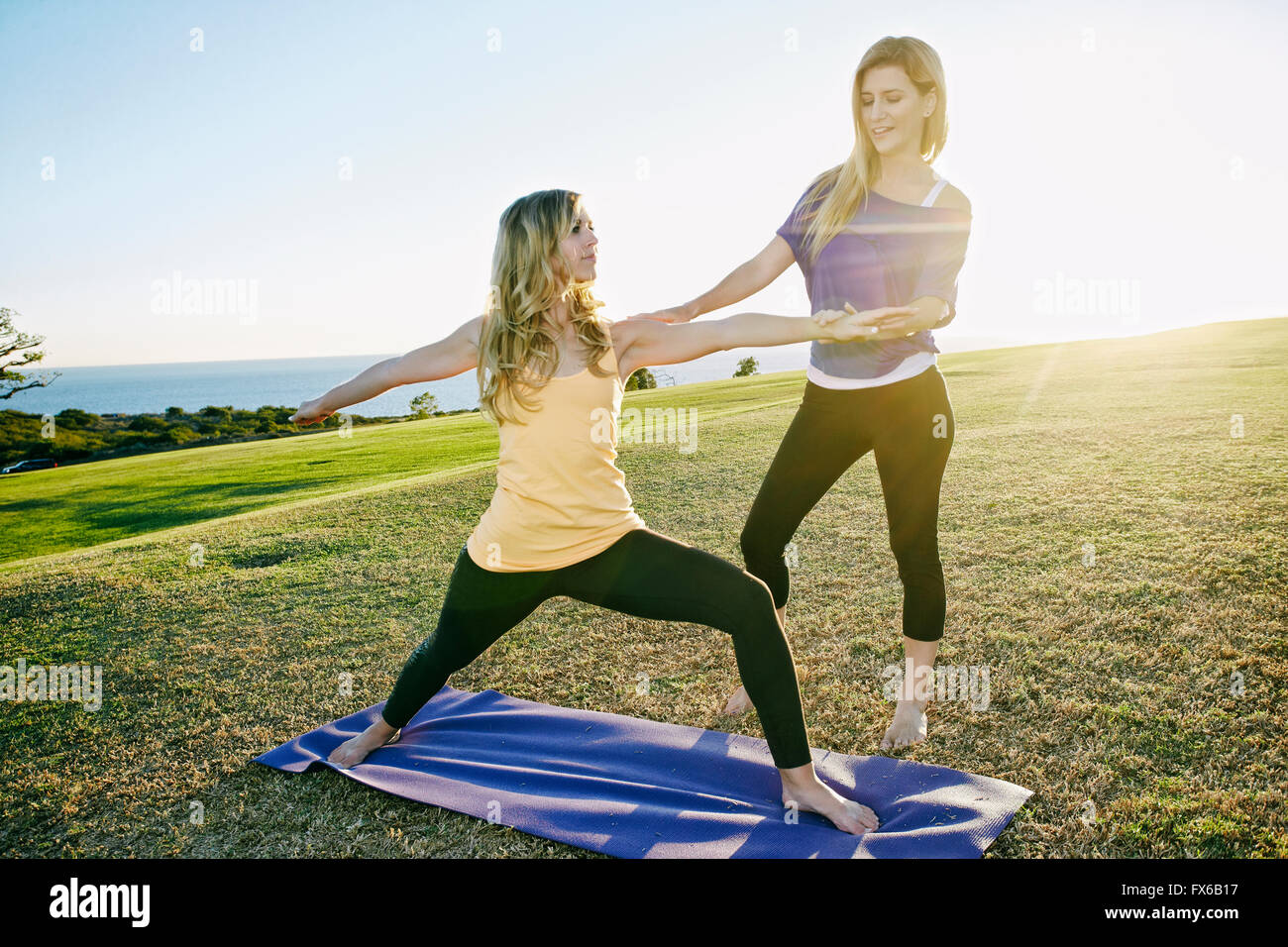 Caucasian woman practicing yoga with trainer in field Stock Photo