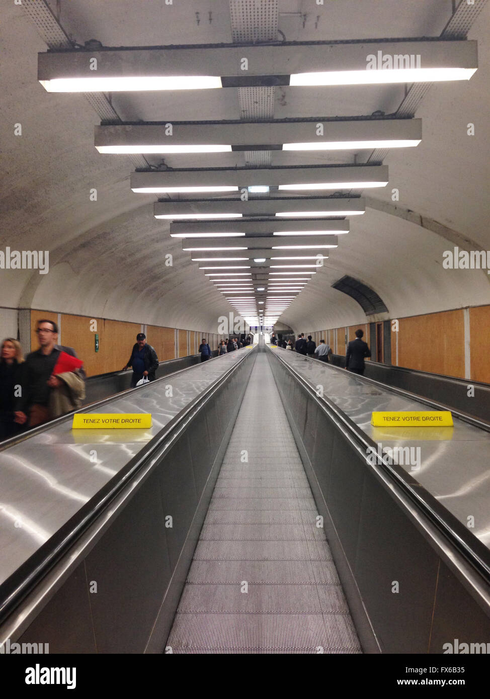 People are riding horizontal escalators in long passage in Chatelet subway station in Paris. Stock Photo