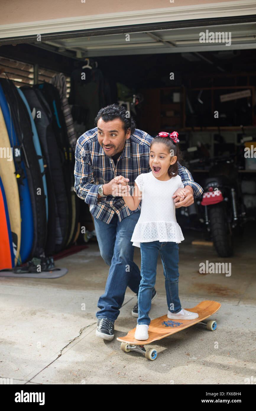 Hispanic father teaching daughter to ride skateboard Stock Photo