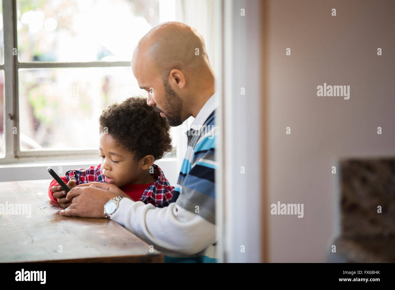 Mixed race father and son using cell phone at table Stock Photo