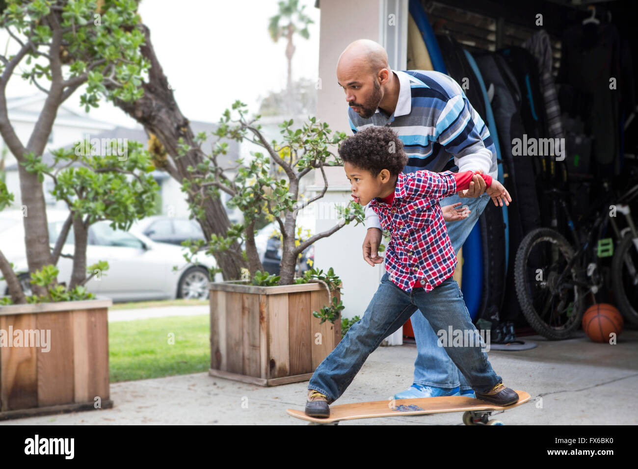 Mixed race father teaching son to ride skateboard outdoors Stock Photo
