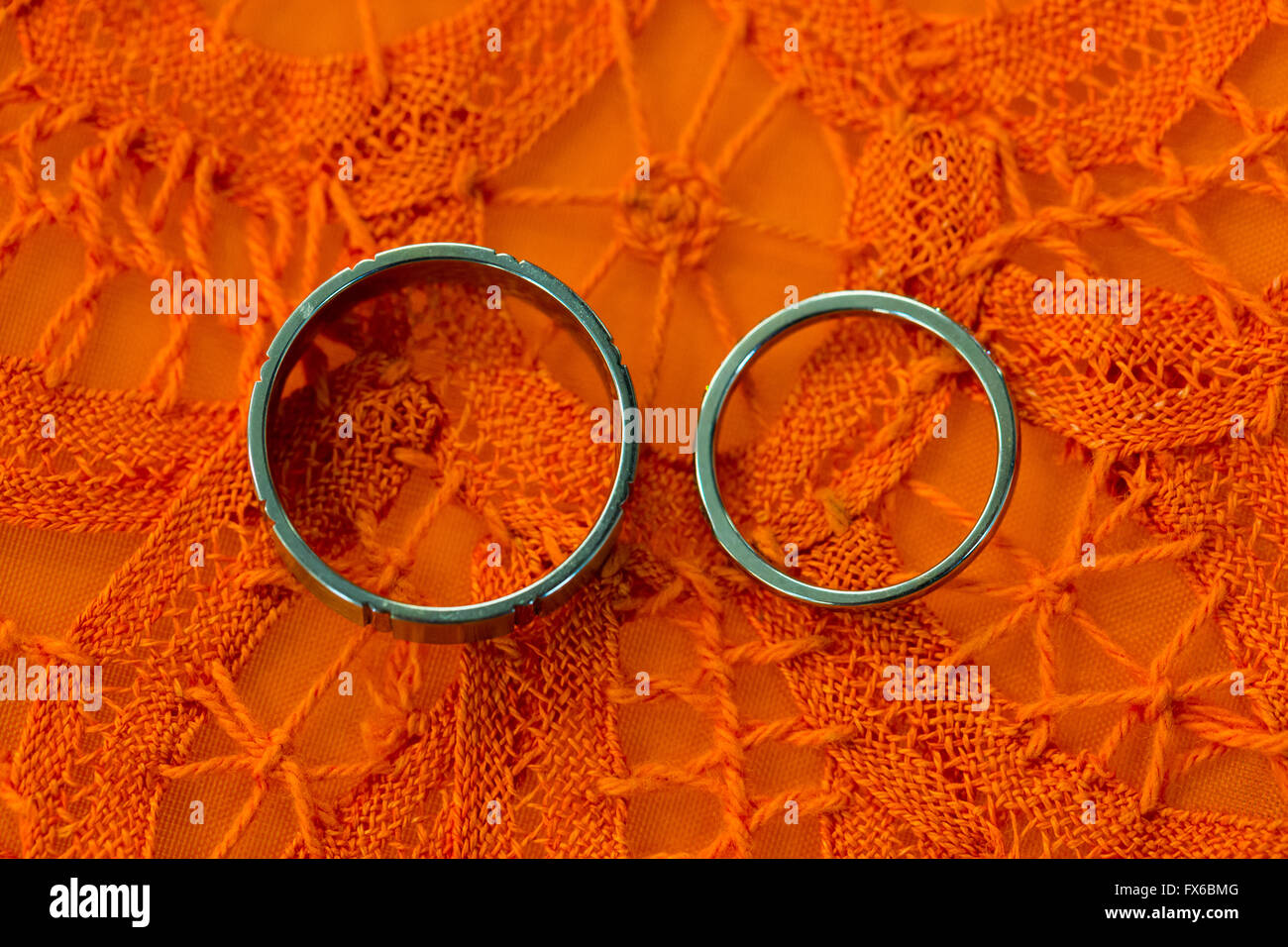 Bride and groom wedding rings photographed before the ceremony on an orange tablecloth. Stock Photo