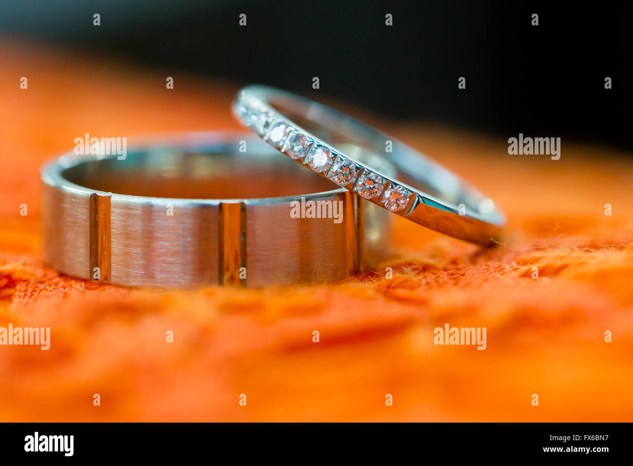 Bride and groom wedding rings photographed before the ceremony on an orange tablecloth. Stock Photo