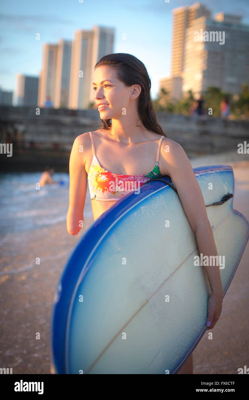 Mixed race amputee carrying surfboard on beach Stock Photo