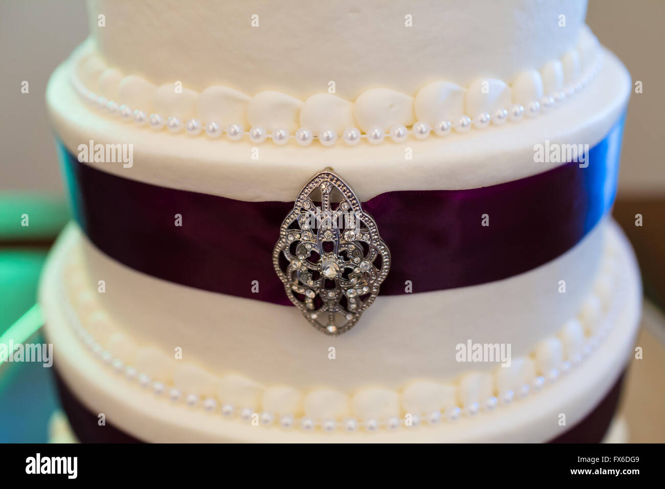 Tall white wedding cake wrapped in purple ribbon with brooches attached to  each tier of the dessert Stock Photo - Alamy, image size:1300x956