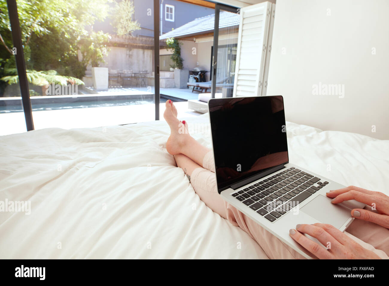 Closeup image of woman relaxing in bedroom and surfing internet on her laptop. Woman sitting on bed and working on her laptop co Stock Photo