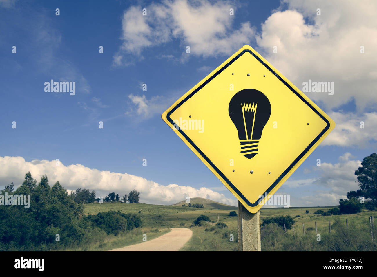 Bright idea light bulb concept icon road sign on empty countryside nature landscape, vintage filter effect. Stock Photo