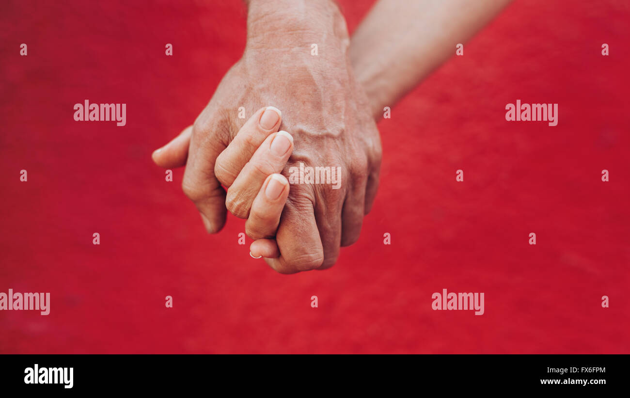 Close up of man and woman holding hands against red background. Affectionate couple holding hands. Stock Photo