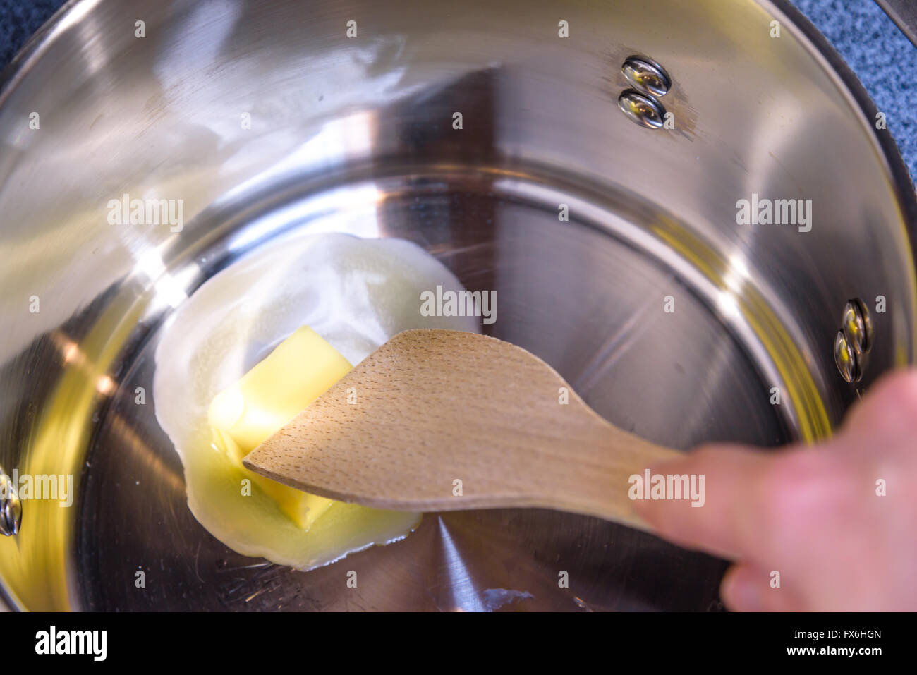 Melting butter in a pan, hand stirring with wooden utensil Stock Photo