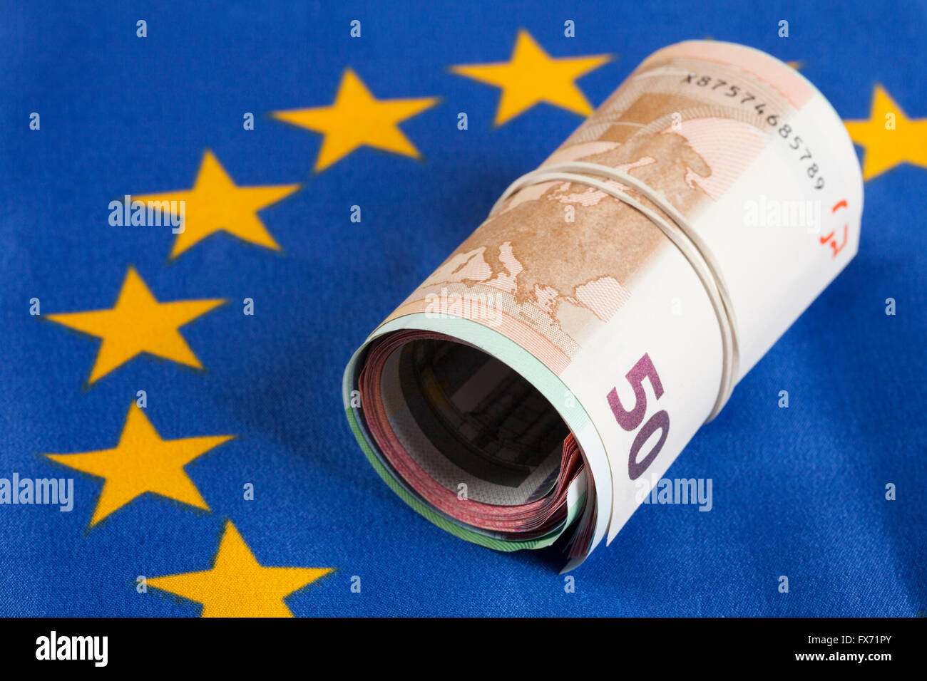 Roll of money with rubber band, multiple bank notes, Euros on European flag Stock Photo