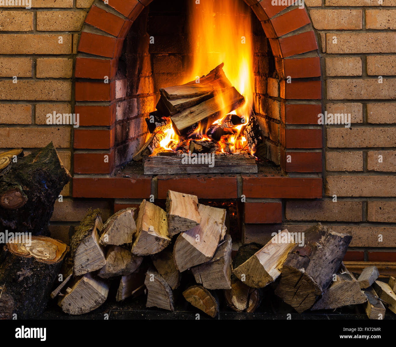 stack of wood and burning wood in indoor brick fireplace in country cottage Stock Photo