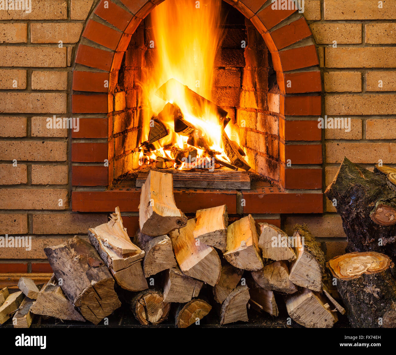stack of firewood and fire in indoor brick fireplace in country cottage Stock Photo