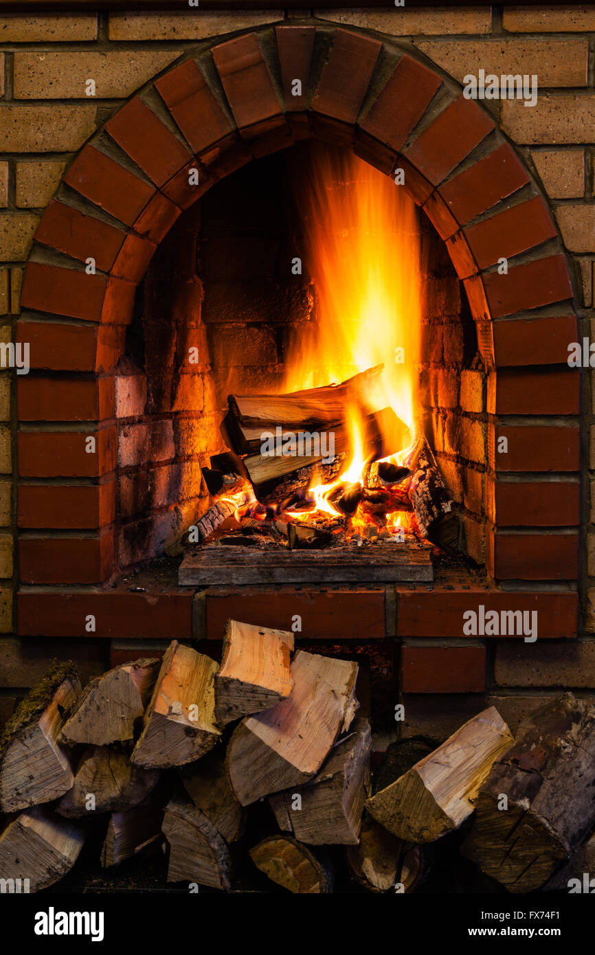 wood stack and logs burning in indoor brick fireplace in country cottage Stock Photo