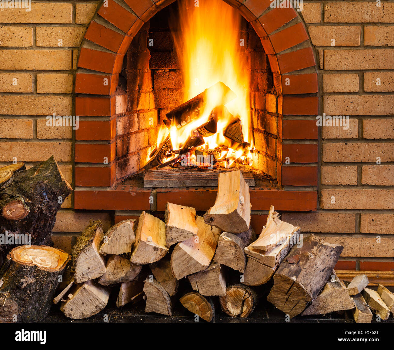 pile of firewood and fire in indoor brick fireplace in country cottage Stock Photo
