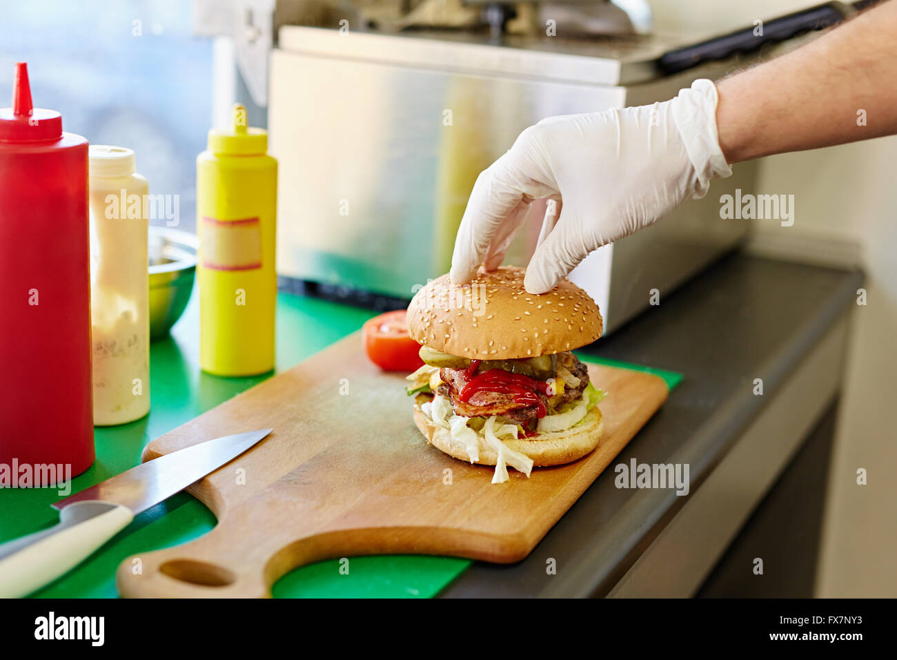 Gloved hand putting the top bun on a delicious burger Stock Photo