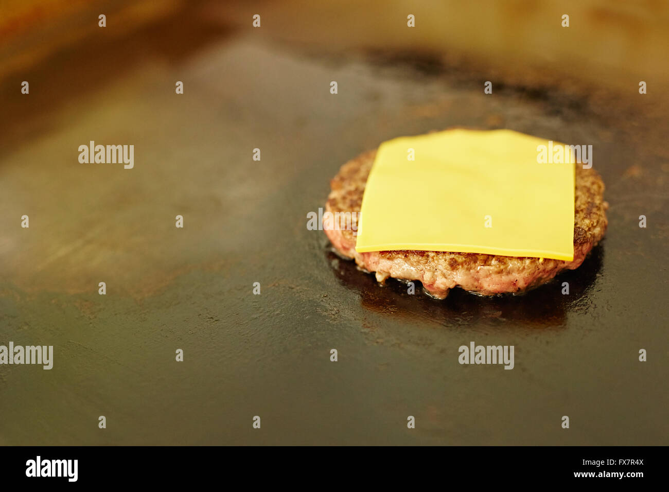 Hamburger patty frying on a grill with fresh cheese Stock Photo