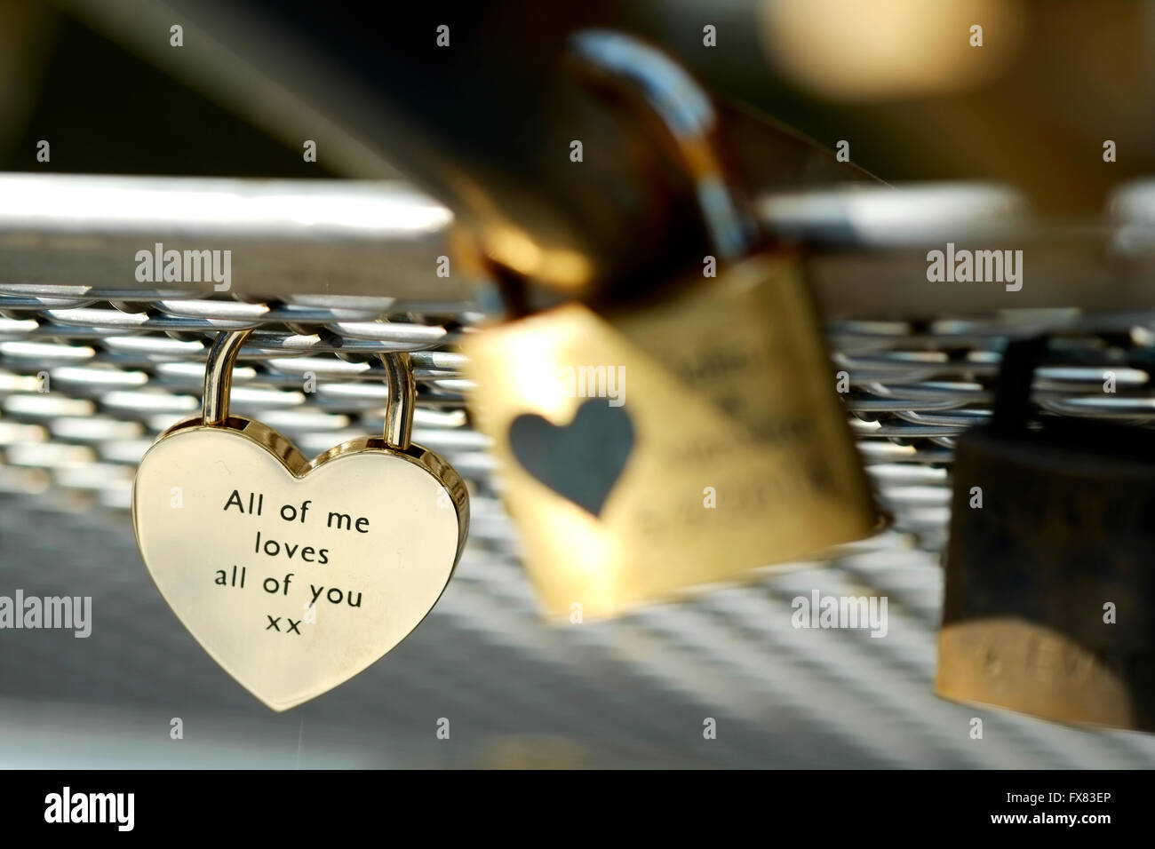 A love lock attached to a wire mesh on a city bridge with a romantic love message etched into the lock Stock Photo