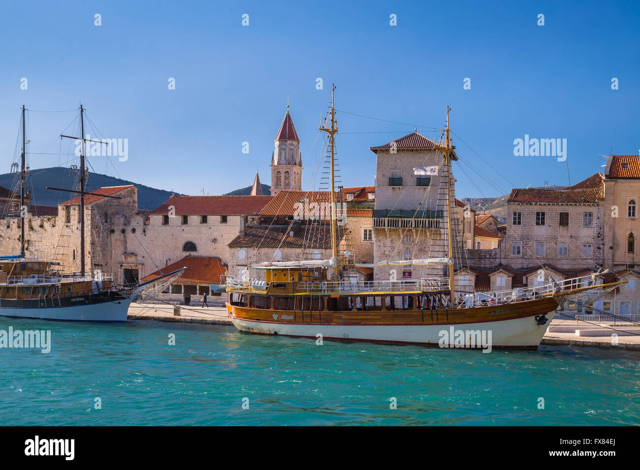 Two large sailing boats are moored along the quayside in Trogir, Crotis. In the background can be seen the bell tower Stock Photo