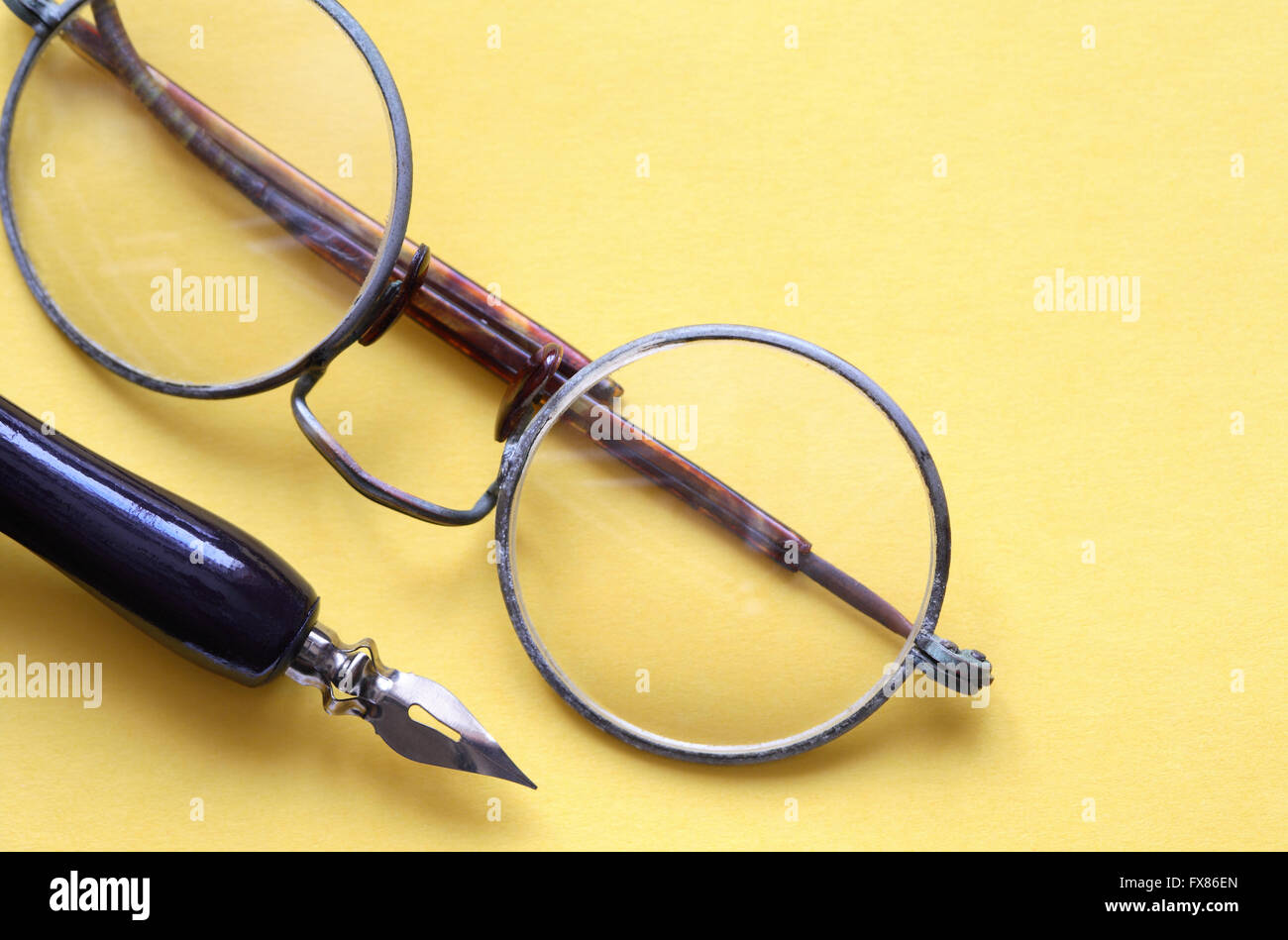Old vintage spectacles near pen on yellow paper background Stock Photo