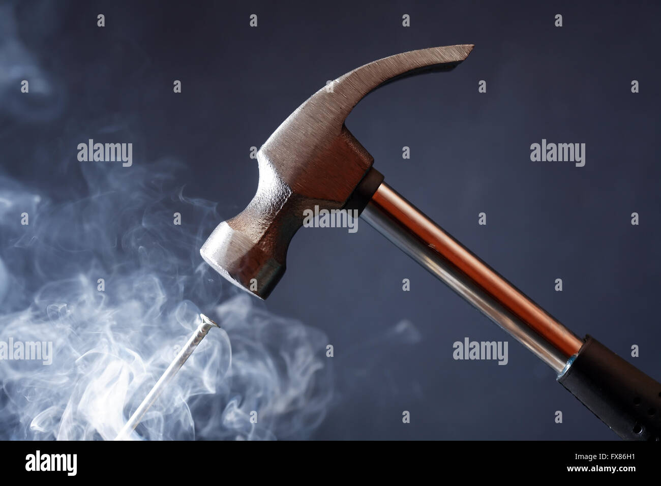 Work tool. Metal hammer above nail with smoke on nice dark background Stock Photo