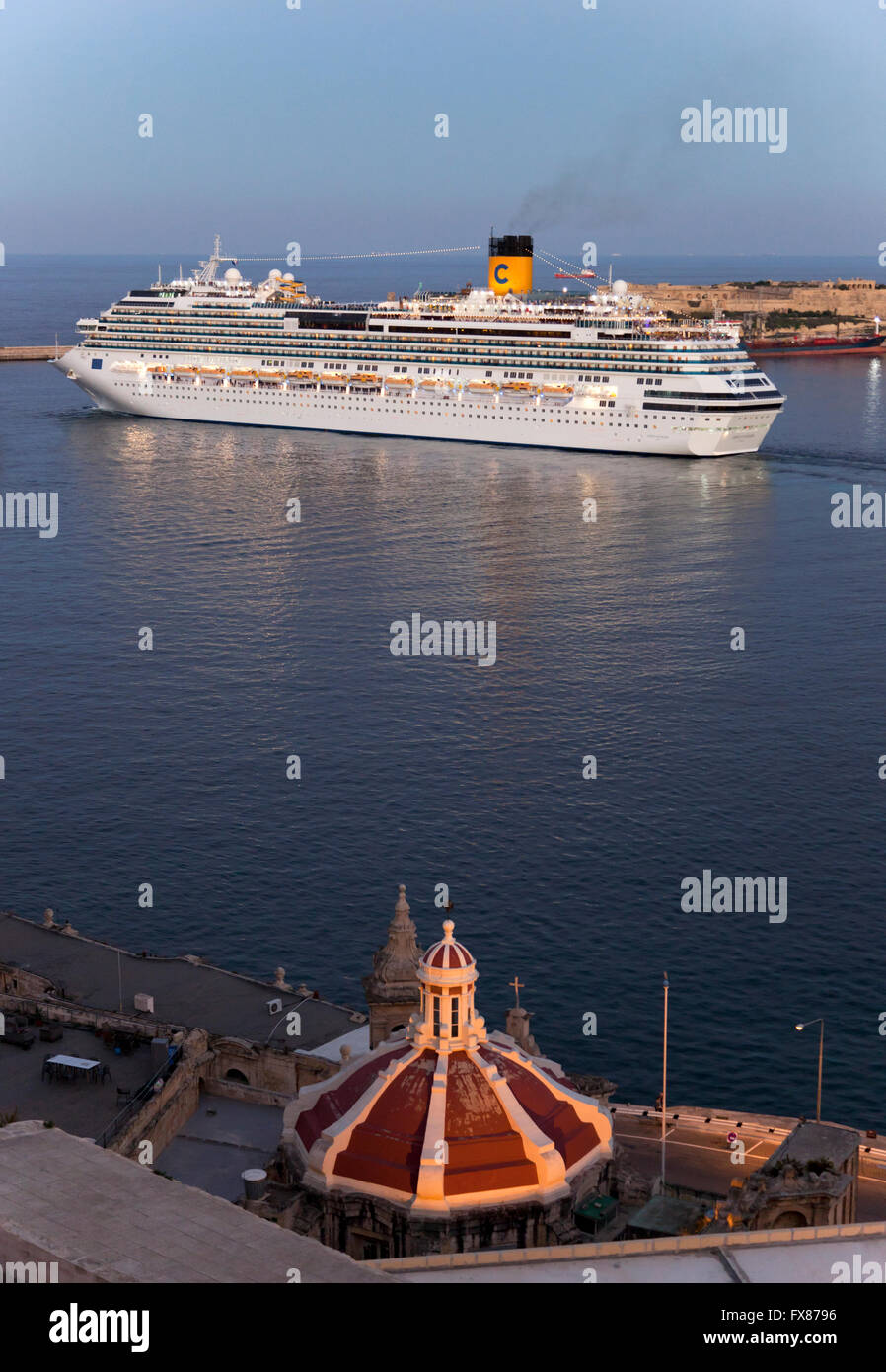 A cruise ship sailing out of the Grand Harbour in Malta past the dome of a Catholic church built on the shore of Valletta. Stock Photo