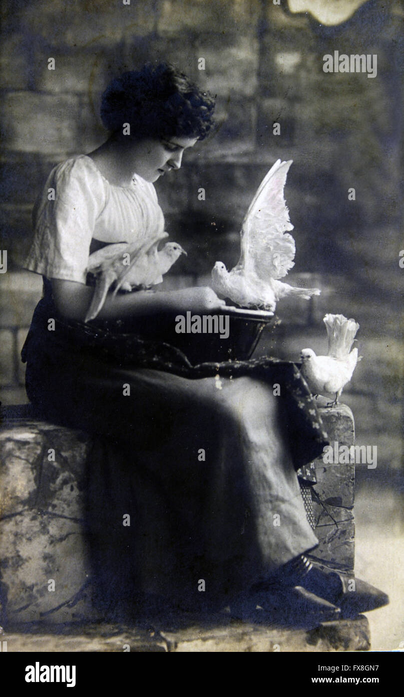 GERMANY - CIRCA 19100: Postcard printed in the Germany shows Woman sitting on stone steps, feeding white doves Stock Photo