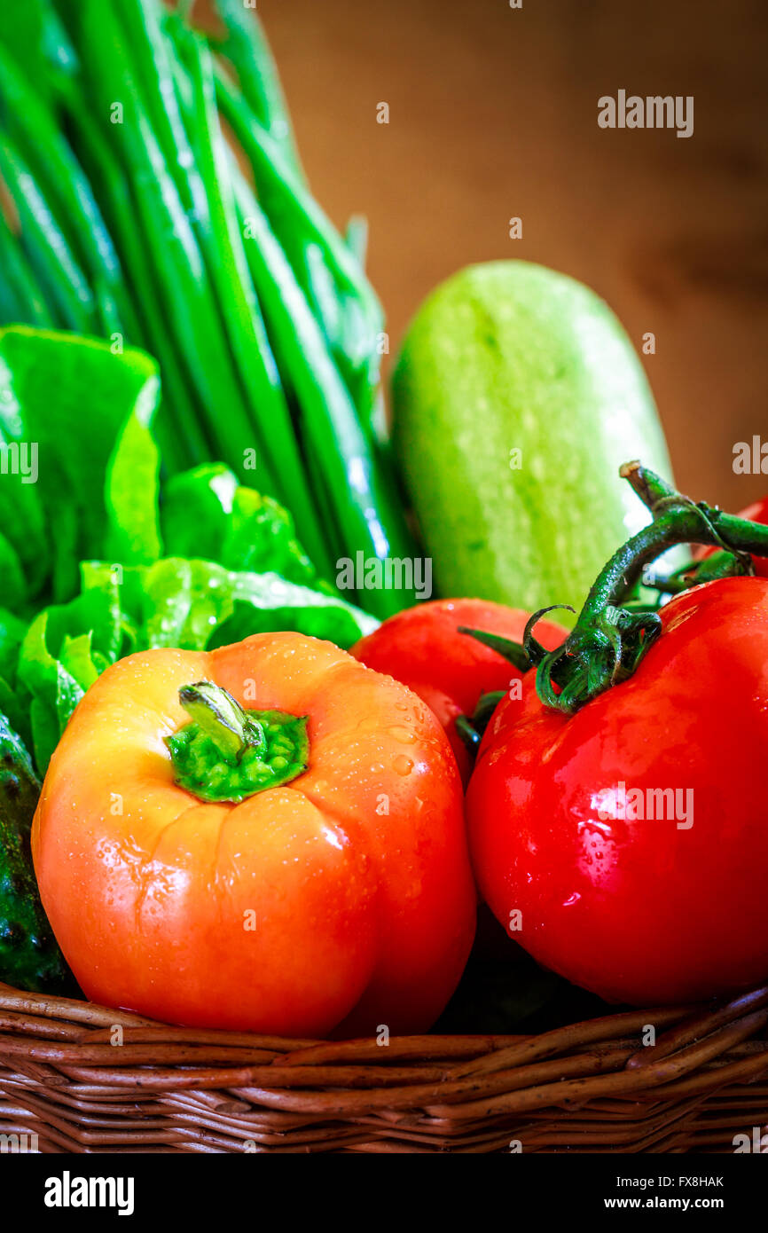 Fresh vegetables in weaved basket on brown background. Focus on bell pepper and tomato. Stock Photo