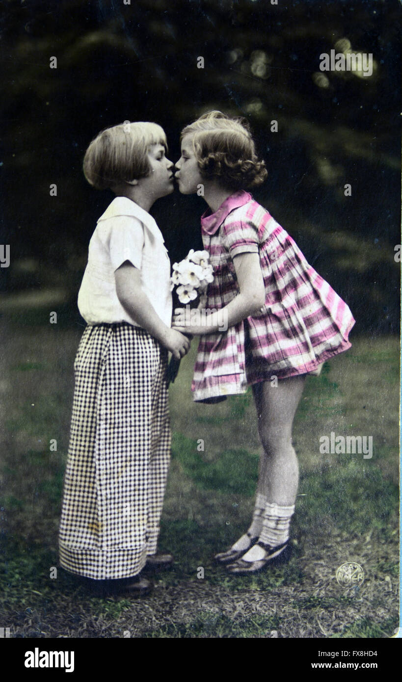 Postcard printed in the Germany shows boy kisses girl, circa 1910 Stock Photo
