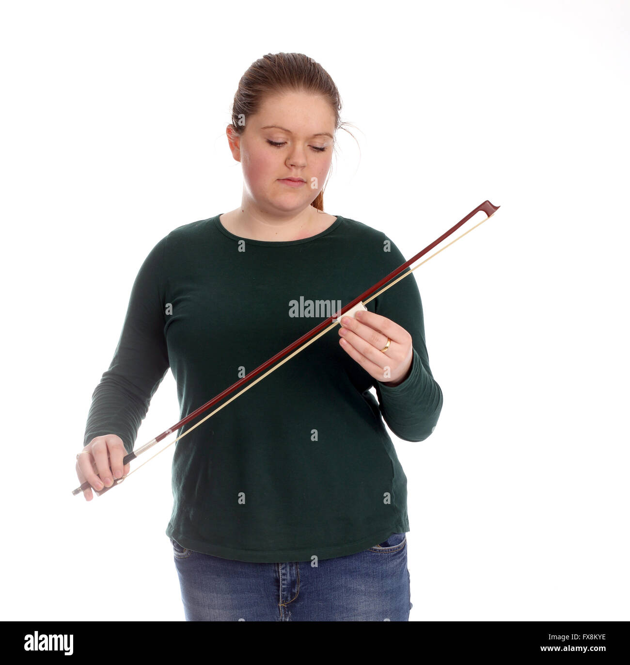 Pretty young woman in a green sweater waxing her violin bow. Stock Photo