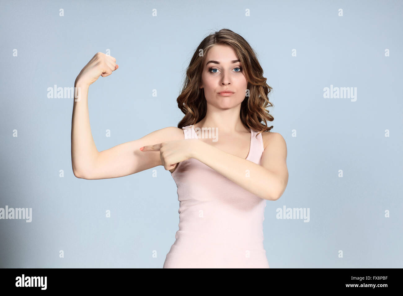 The young woman showing her muscles on gray background. Stock Photo