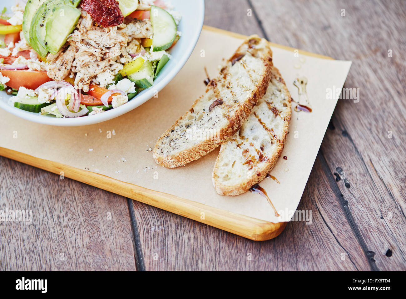 Freshly sliced baguette alongside a fresh salad on wooden board Stock Photo