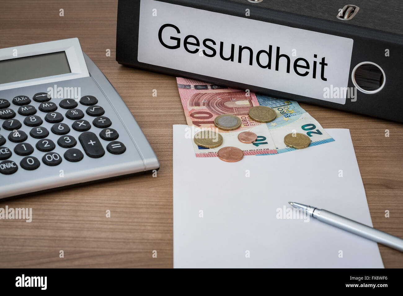 Gesundheit (German Health) written on a binder on a desk with euro money calculator blank sheet and pen Stock Photo