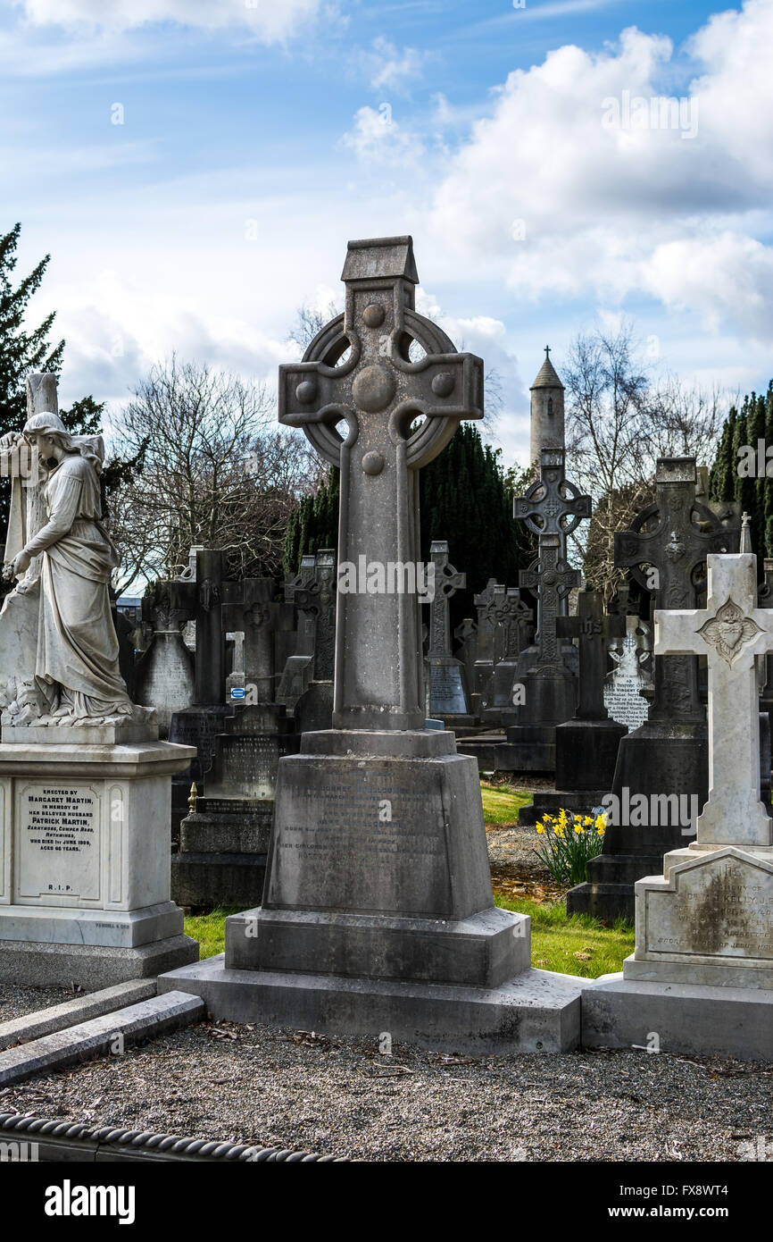 A stonework Celtic cross stands over a grave in Glasnevin cemetery in Dublin with Daniel O'Connell tower in background. Stock Photo