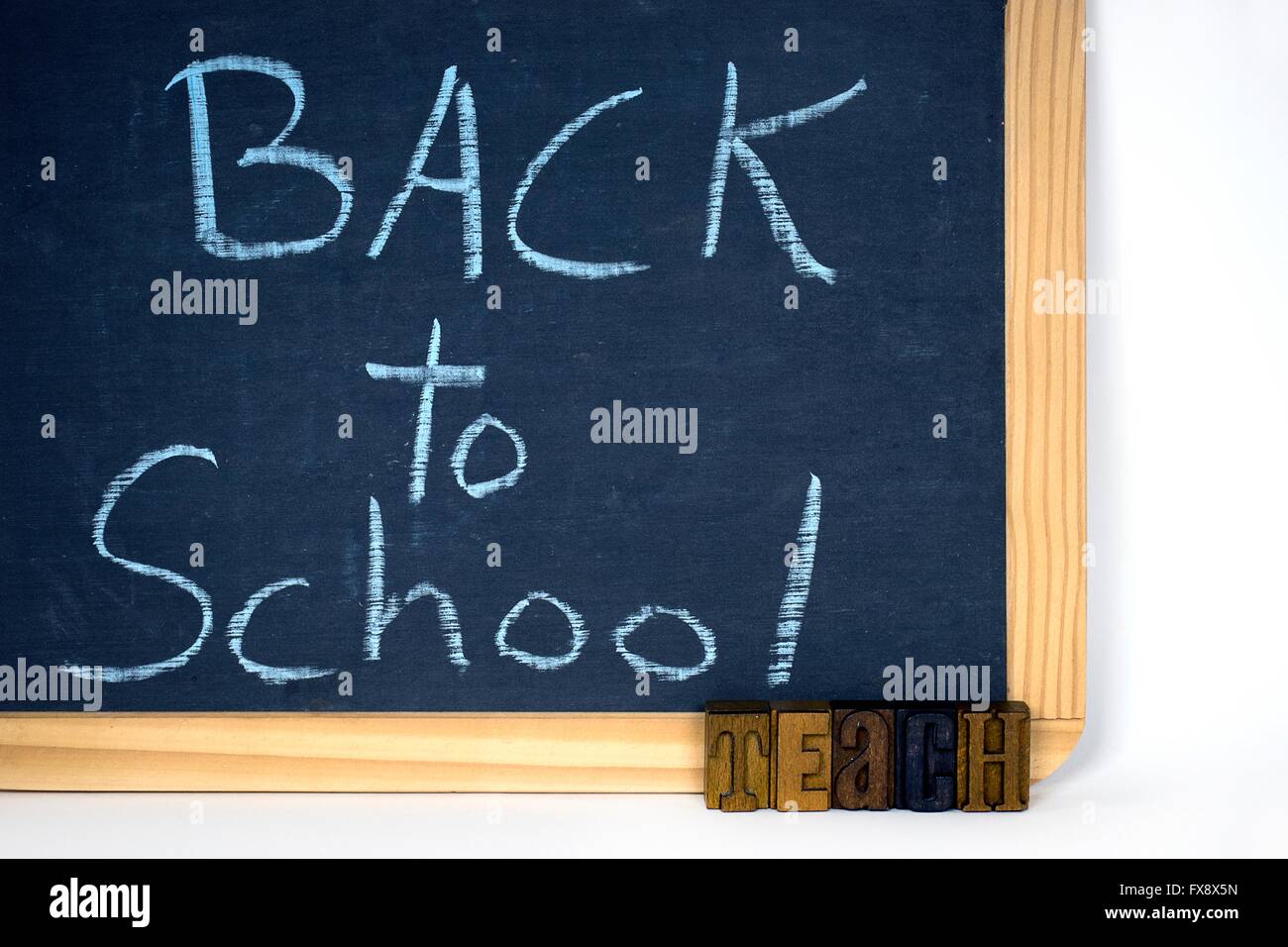 Back to school sign on a dusty black chalkboard with word 'teach' in vintage wooden letterpress type. Stock Photo