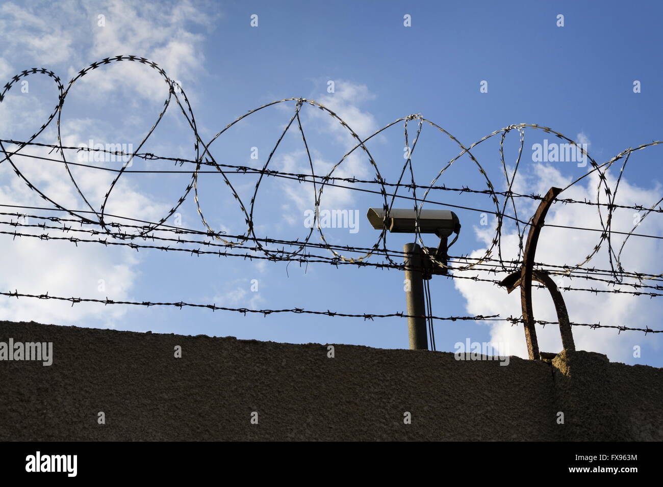 Prison wall barbed wire fence detail with blue sky in background Stock
