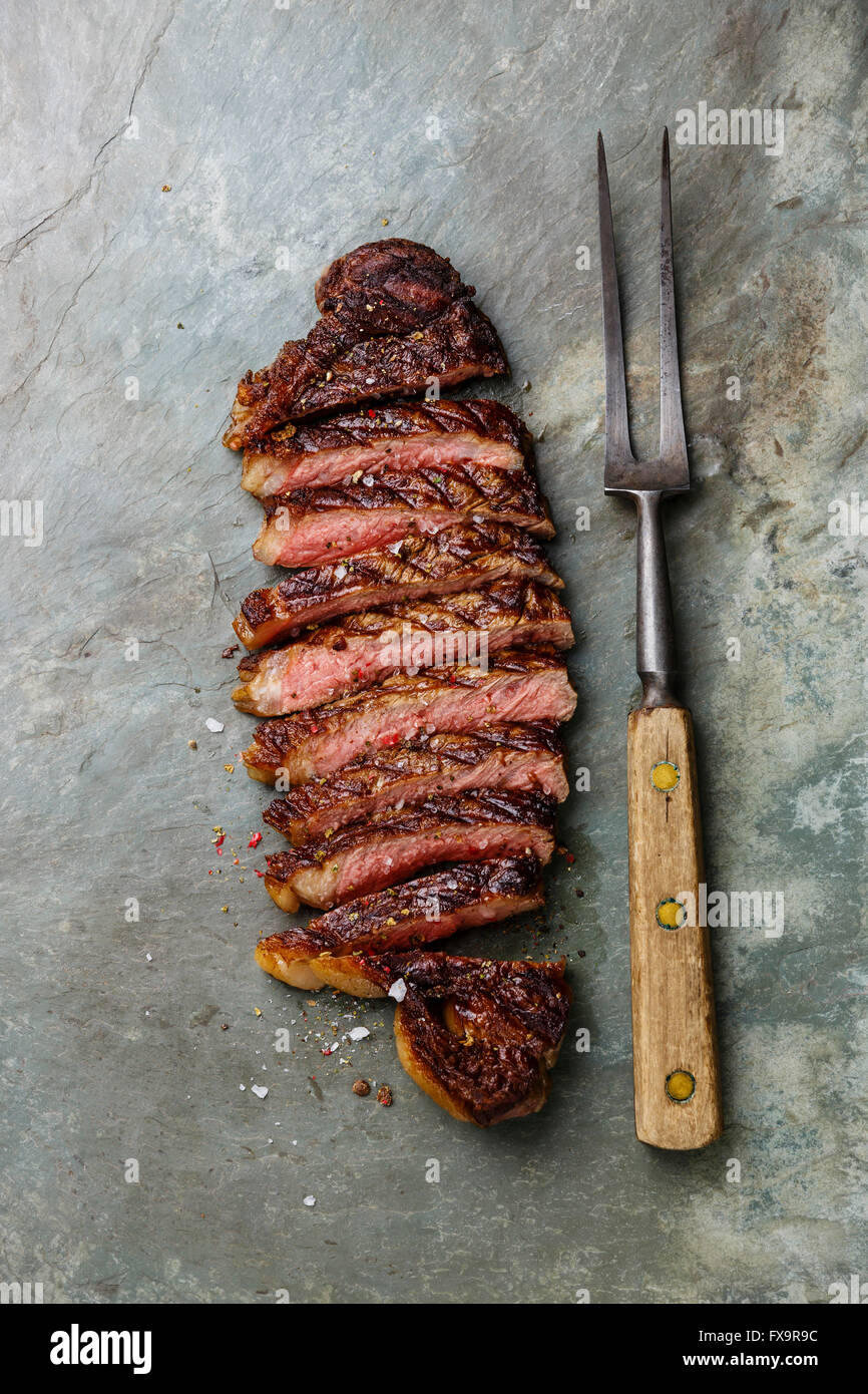 Sliced grilled beef barbecue Striploin steak and meat fork on gray stone slate background Stock Photo