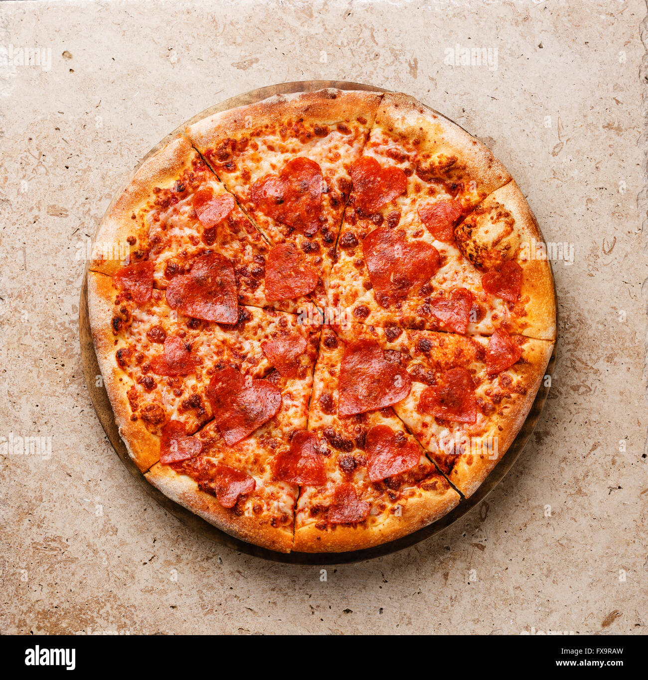 Heart shape sliced Pepperoni Pizza on stone travertine background Stock Photo