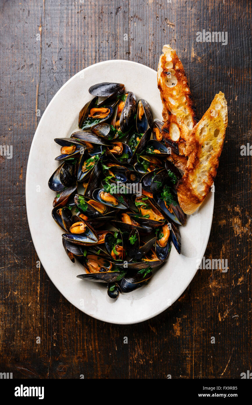 Mussels with parsley and bread toasts on plate on dark wooden background Stock Photo
