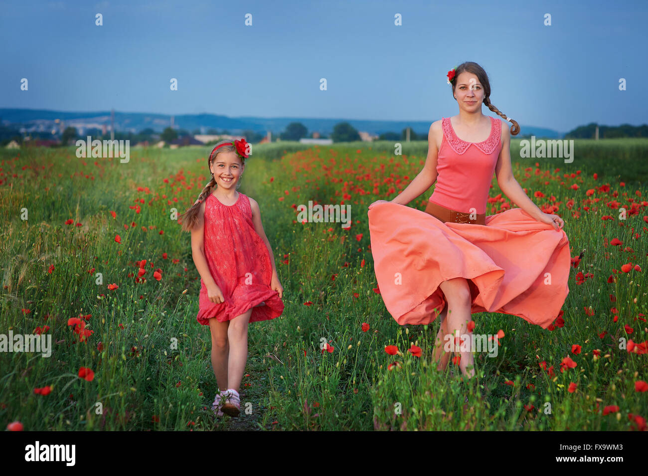 two girls in red dress walking on poppy field Stock Photo - Alamy