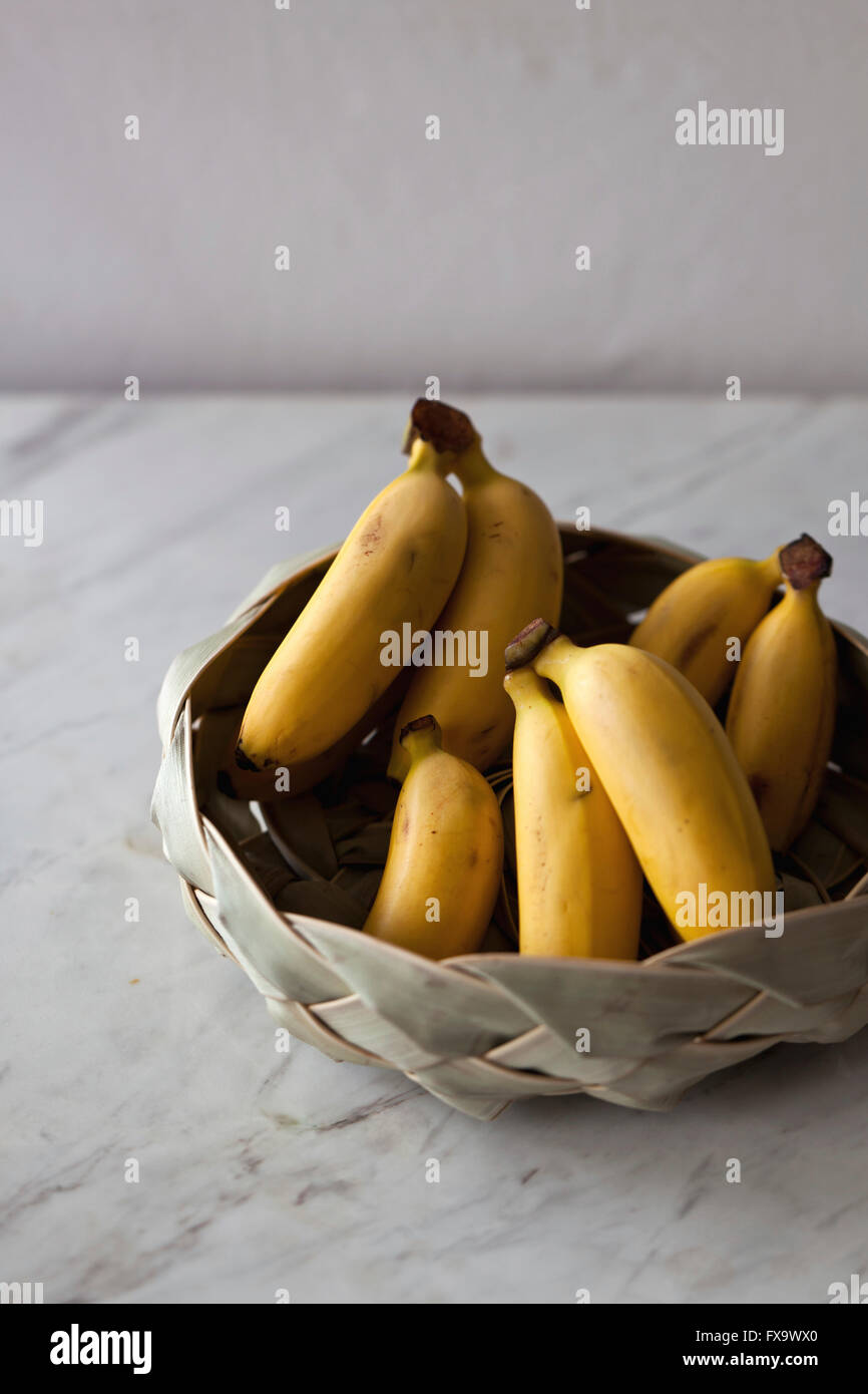 Baby bananas in the basket on the white marble table Stock Photo