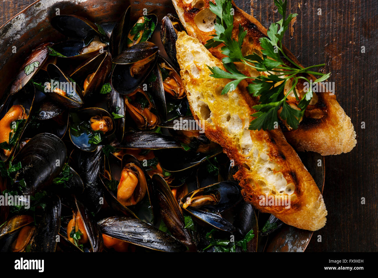 Mussels with parsley and bread toasts on dark background close up Stock Photo