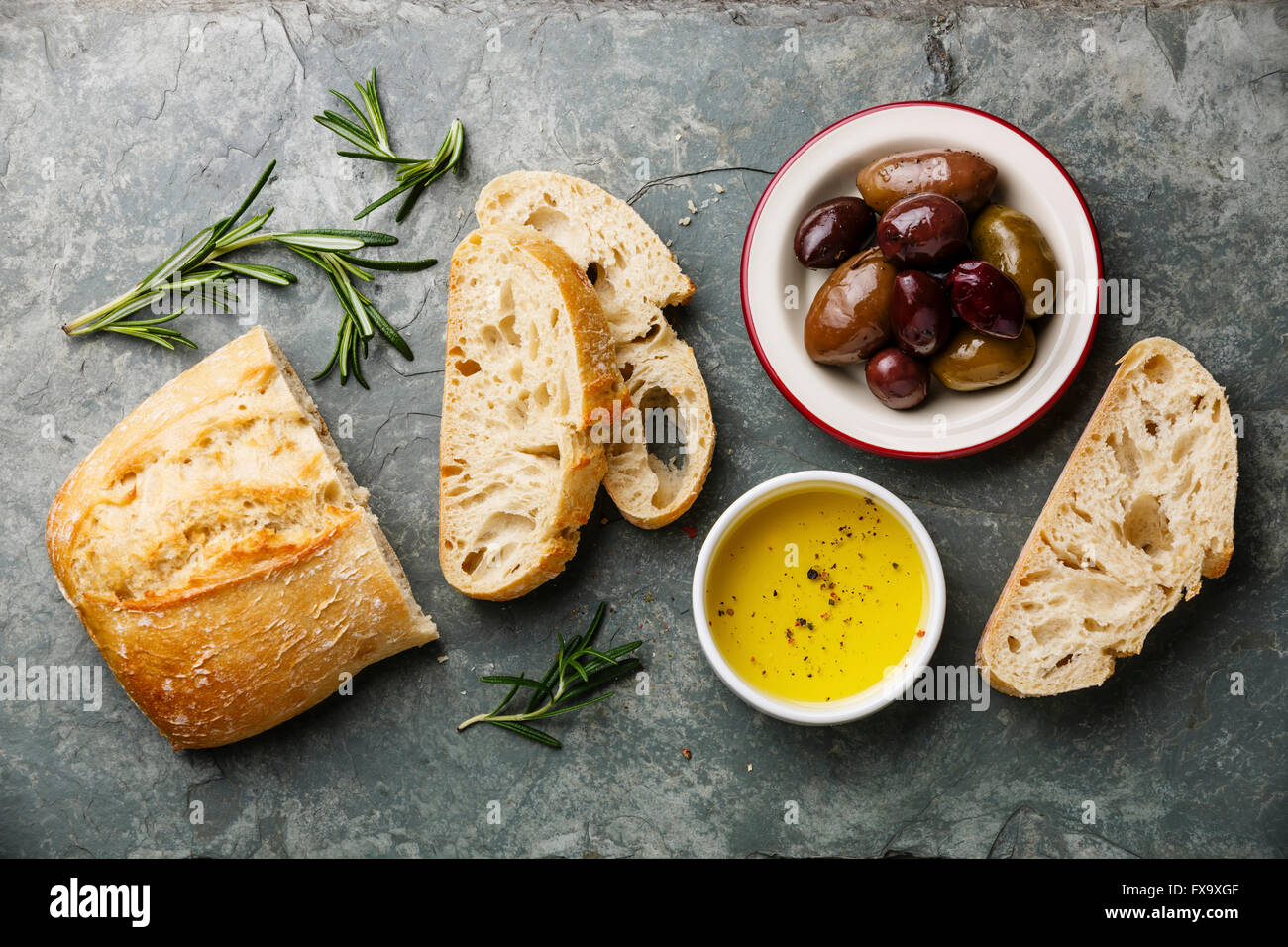 Sliced fresh bread Ciabatta with olive oil, olives and rosemary on gray stone slate background Stock Photo
