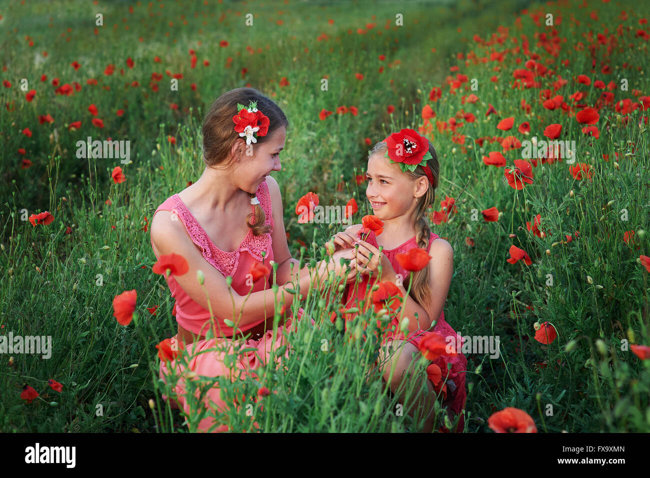 two girls in red dress walking on poppy field Stock Photo - Alamy
