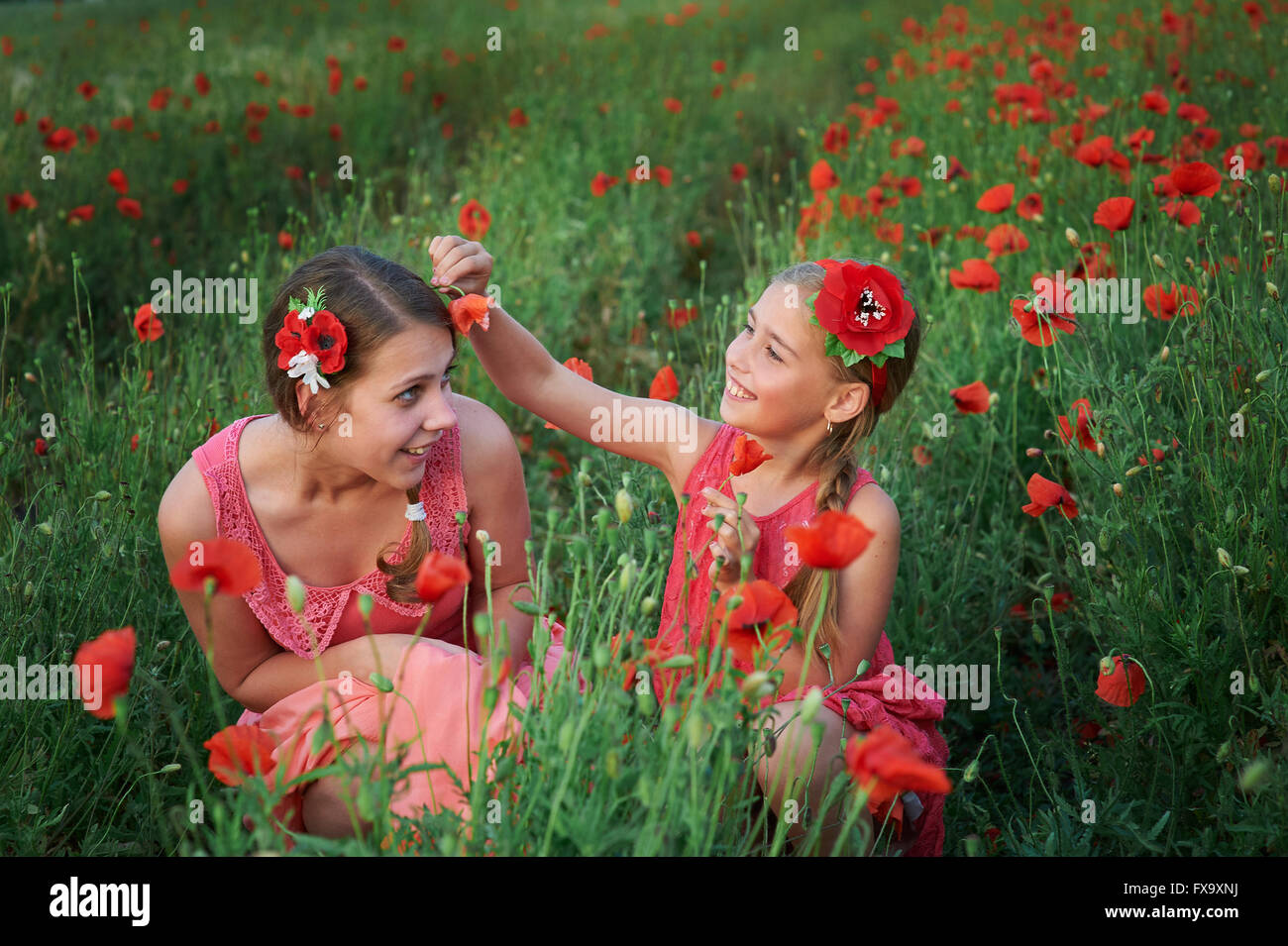 two girls in red dress walking on poppy field Stock Photo - Alamy