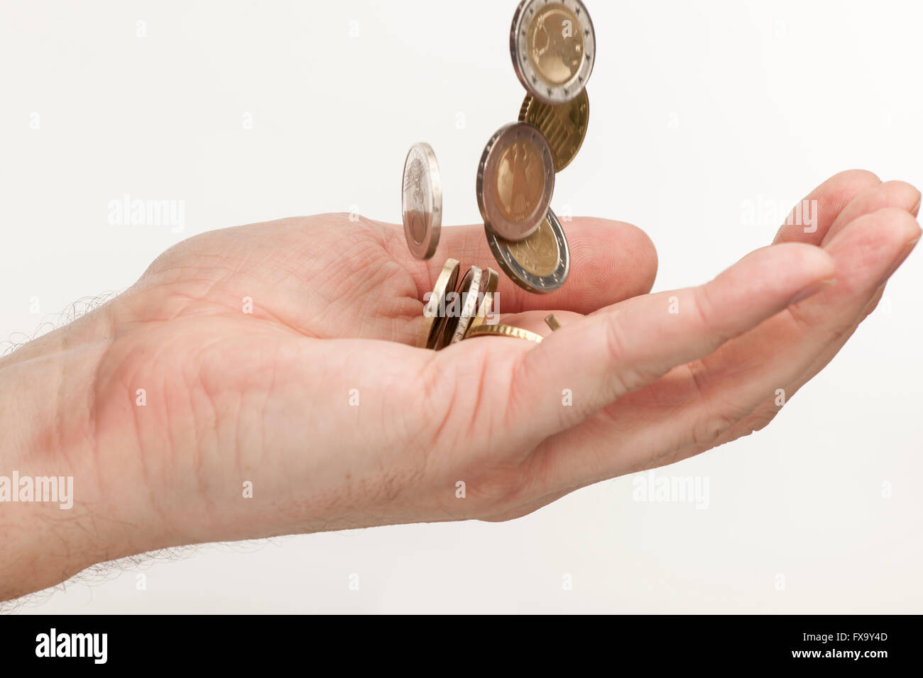 side detail view in a male hand of falling EURO coins against a white ...