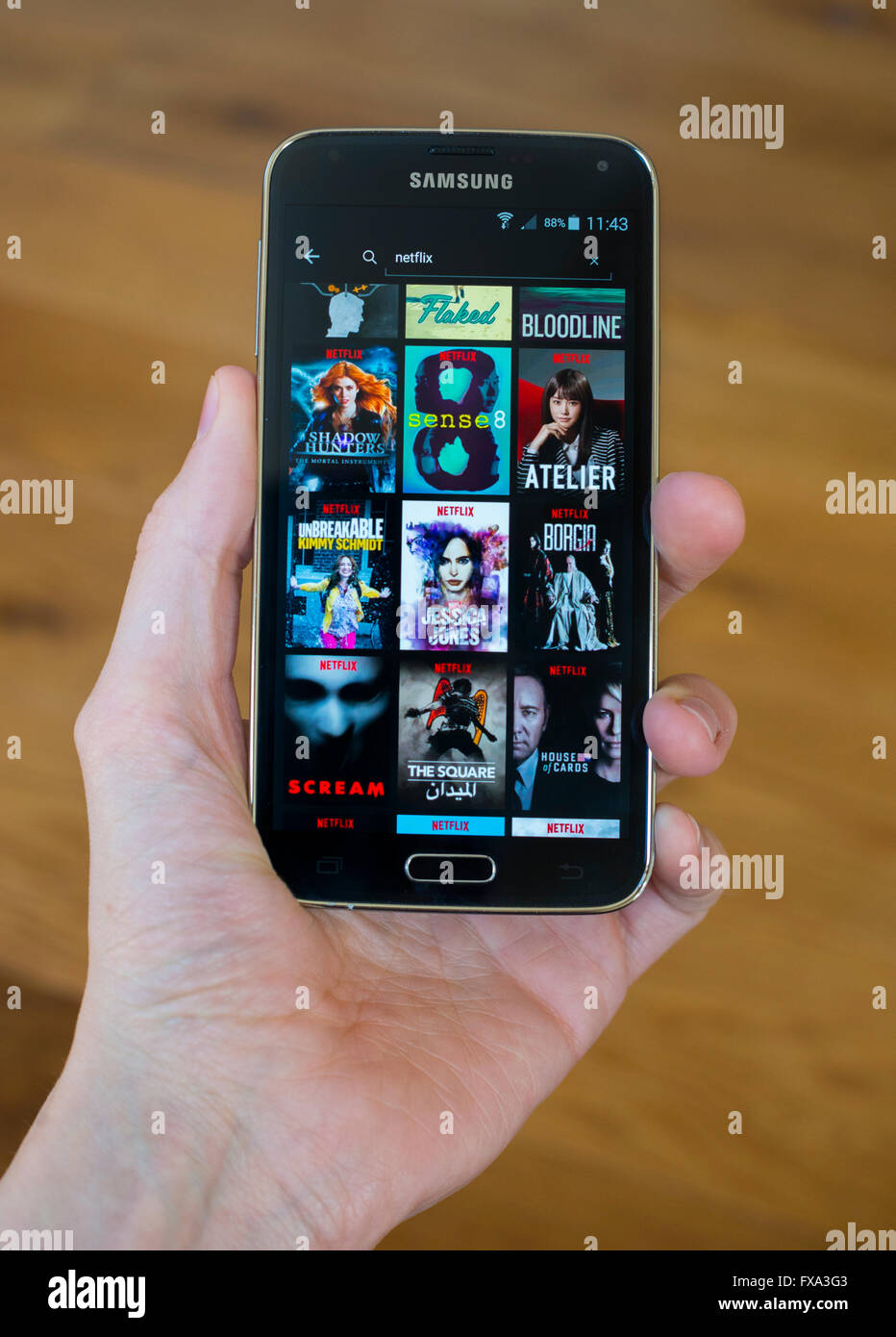 A hand holding a Samsung phone with the Netlfix app open, showing original Netflix content. Stock Photo