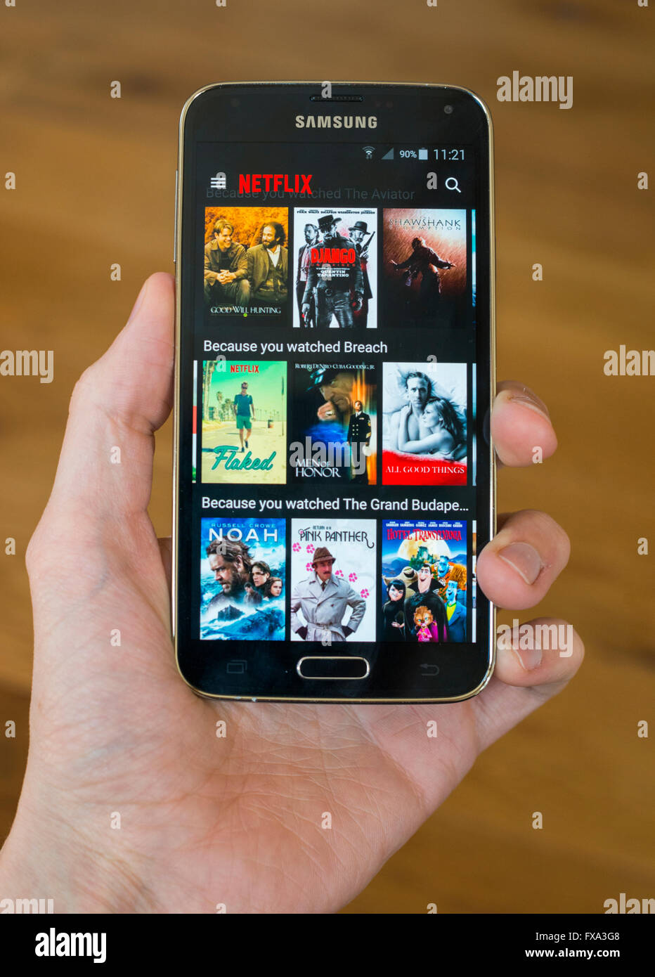 A hand holding a Samsung S5 phone with the Netlfix app open, showing tv shows and films available to watch. Stock Photo